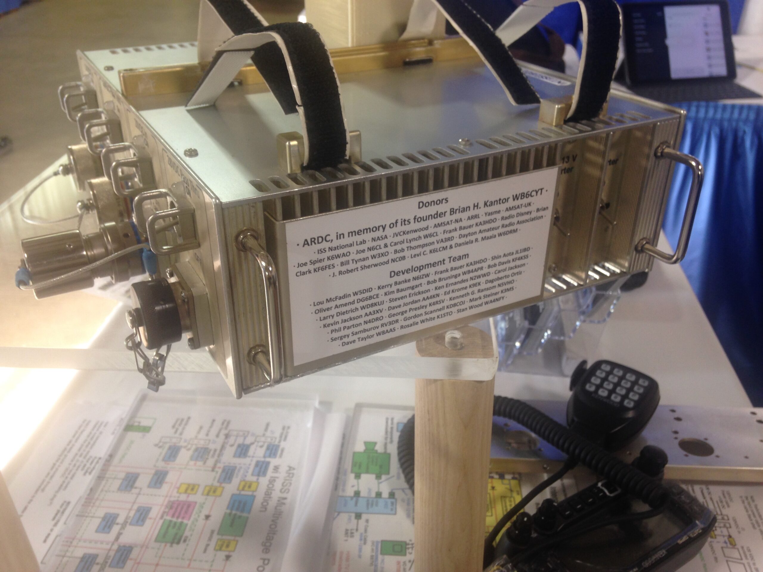 Model of the Amateur Radio on the International Space Station (ARISS) power supply with a placard honoring the donors that made the CRS-20 mission possible, including Brian Kantor, WB6CYT